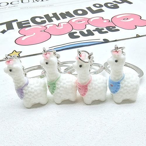 Four flocked alpaca keychains with purple green pink and blue bibs side view
