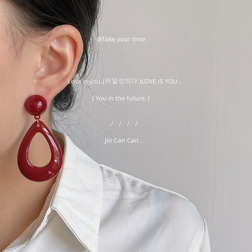 Wine red teardrop drop earring worn on ear white shirt