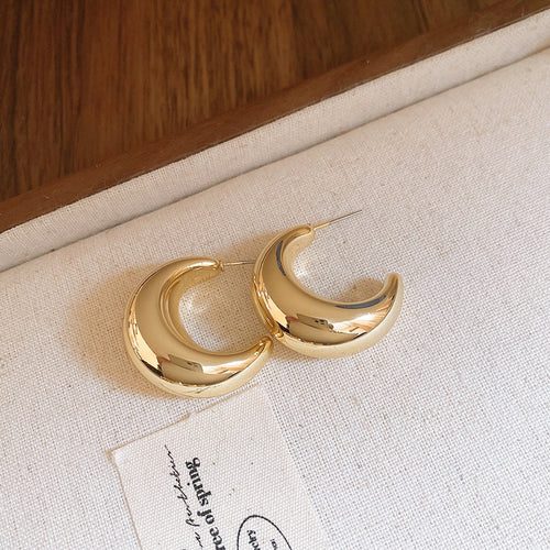 Five variations of smooth sculptural gold-tone teardrop hoops shown worn at the ear.