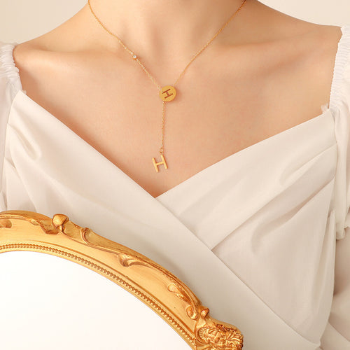 Gold letter H Y-lariat necklace worn with white dress