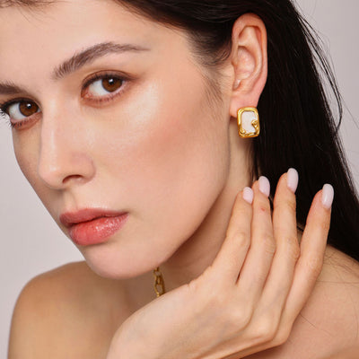 Model wears gold rectangular white enamel scroll stud earring