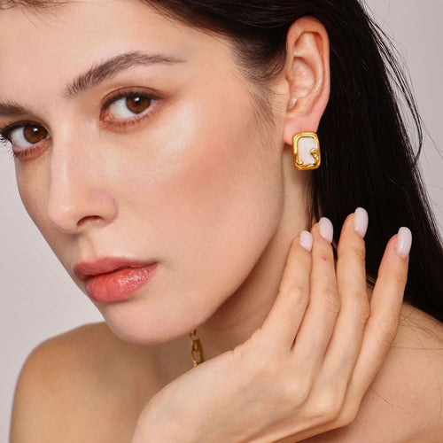 Model wears gold rectangular white enamel scroll stud earring