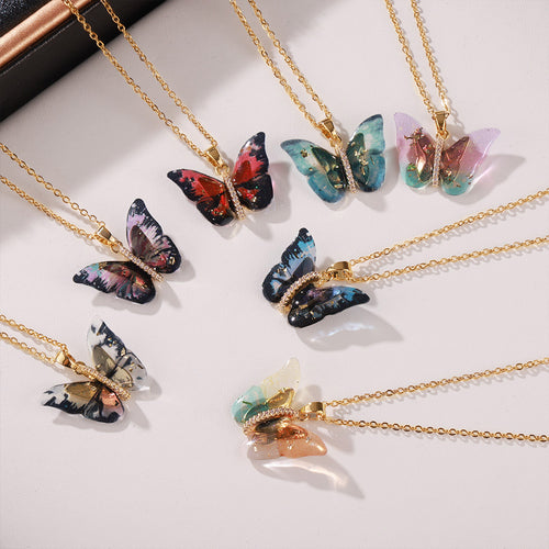 Flat lay of seven multicolor resin butterfly pendants on gold chains
