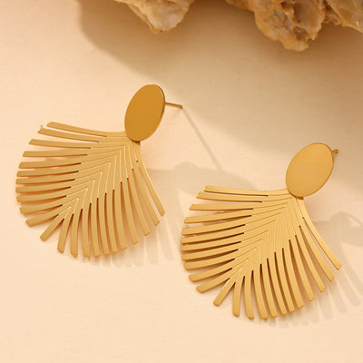 Pair of gold palm leaf fan earrings on beige surface