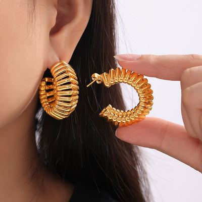 Gold C-shape ribbed hoop earrings worn and held beside model ear
