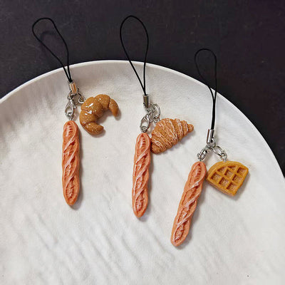 Three mini baguette phone charms with croissant and waffle pairs on white plate