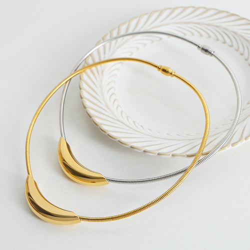 Gold and steel crescent snake chain necklaces coiled on ceramic dish