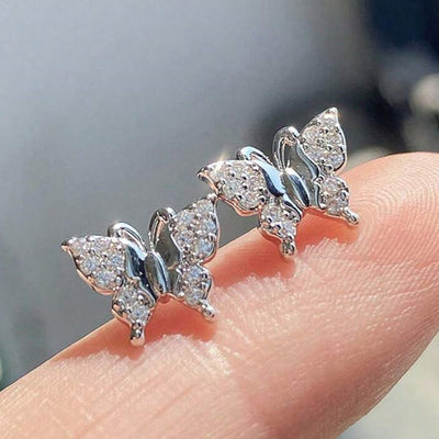 Pair silver pave butterfly stud earrings balanced on fingertip close-up