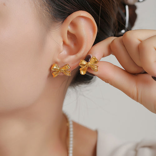 Gold bow stud earring being placed on ear