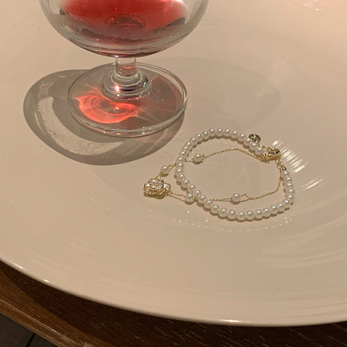 white double-row pearl-like bracelet with a fine chain and flower charm shown in the first close product view