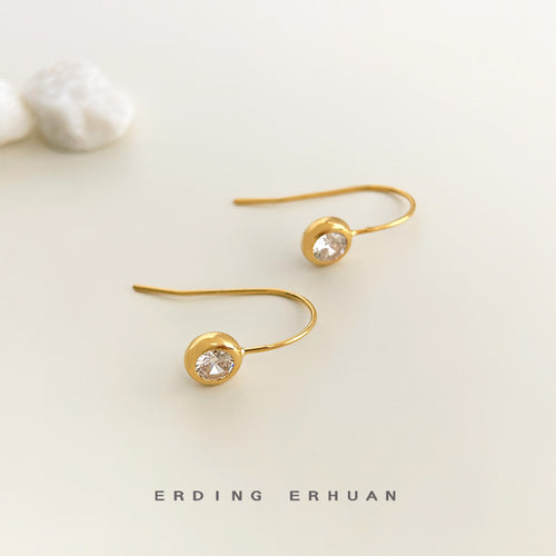 Gold U-hook clear CZ round earrings on cream surface