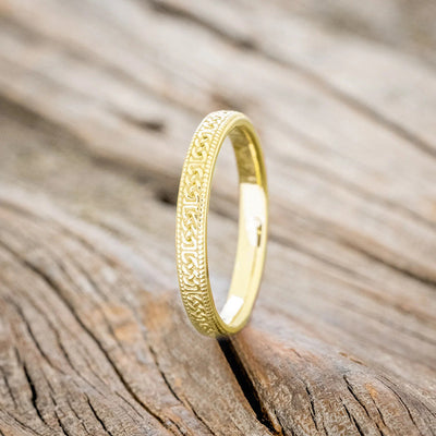 Gold Celtic knot band ring upright side view on wood surface