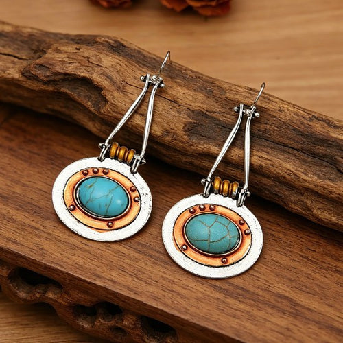 Close view of silver and copper-tone turquoise-color disc drop earrings in warm light