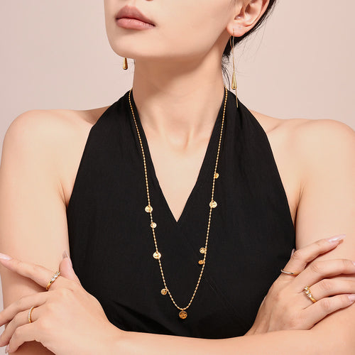 Model in black top wearing long gold hammered disc station necklace layered