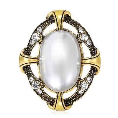 Front view of an oval white cabochon framed by antique-tone curves and crystals