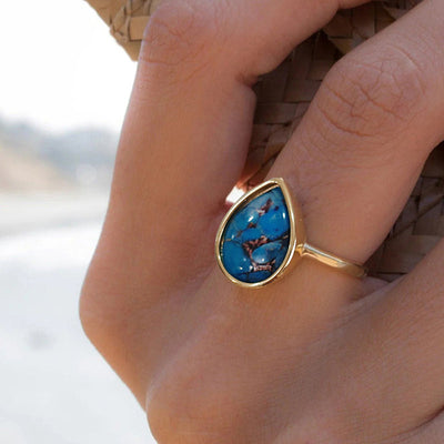 Gold teardrop blue cabochon ring worn on finger outdoors