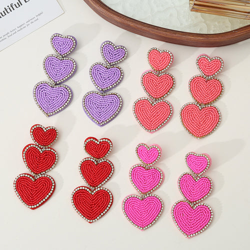 Four pairs of triple heart beaded earrings in purple, coral, red and pink on mirror tray