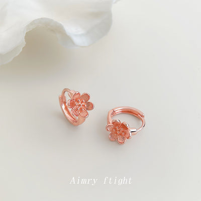 Rose gold mini huggie peach blossom hoops on cream surface