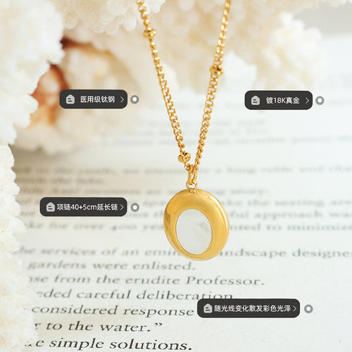 Gold oval shell pendant with material and length labels on book