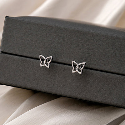 Tiny silver openwork butterfly studs on the edge of a dark gray jewelry box