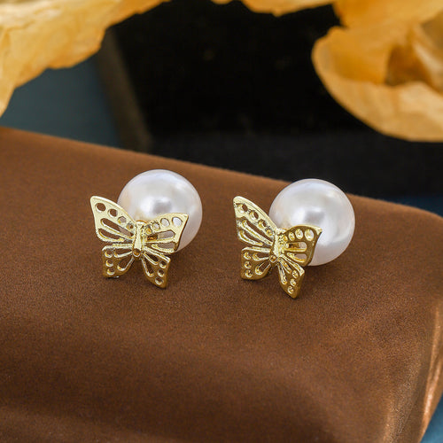 Close pair of butterfly and pearl studs on brown fabric