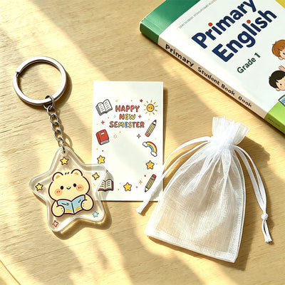 A star bear keychain lies beside a Happy New Semester card and white drawstring pouch.