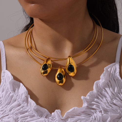 Model wearing three gold teardrop black stone snake chain necklaces layered