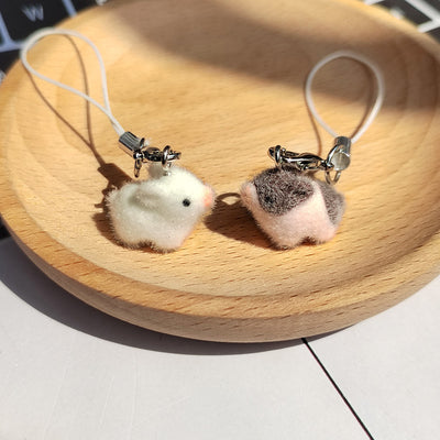 White and brown-patched flocked pig phone charms on wood dish