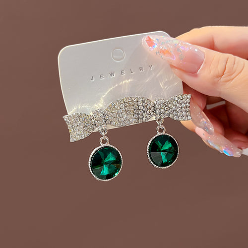 Green crystal bow drop earrings on white jewelry card held by hand