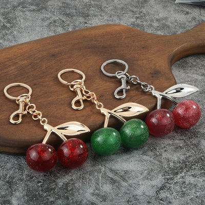 Three glitter cherry keychains in dark red, green and light red with gold- and silver-tone hardware.