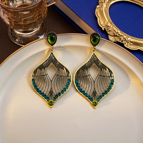 Gold leaf filigree drop earrings with green tops on cream plate