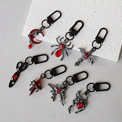 Assorted gothic black keychain charms with red stones on white foam board