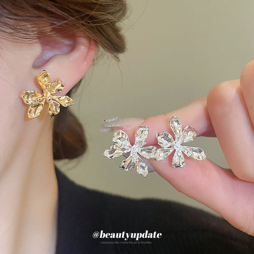 Five-petal sculpted flowers with a polished metal finish shown worn at the ear.