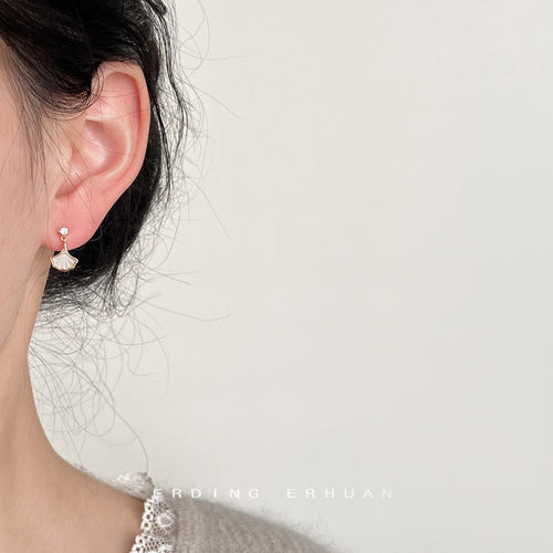 Gold-tone clear-stone-top white-ginkgo-leaf studs shown worn on an ear.