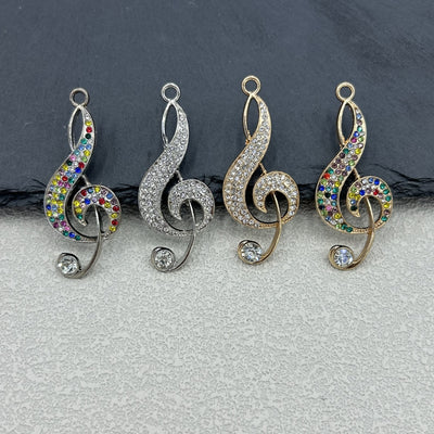 Four treble clef charms in silver rainbow, silver clear, gold clear and gold rainbow rhinestones on a dark background