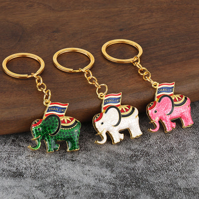 Three Thailand flag elephant keychains in green, white, and pink on a wood surface.