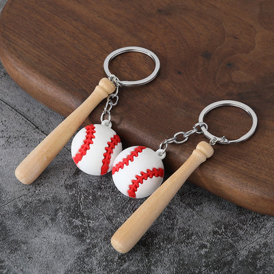 Two baseball-and-bat keychains displayed on a dark wood surface.