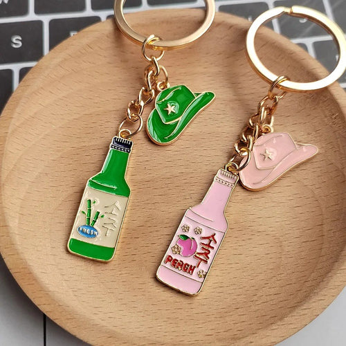 Both soju bottle and hat keychain sets close-up on wooden dish over keyboard