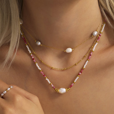 Model wearing layered pink natural stone pearl and gold chain necklaces