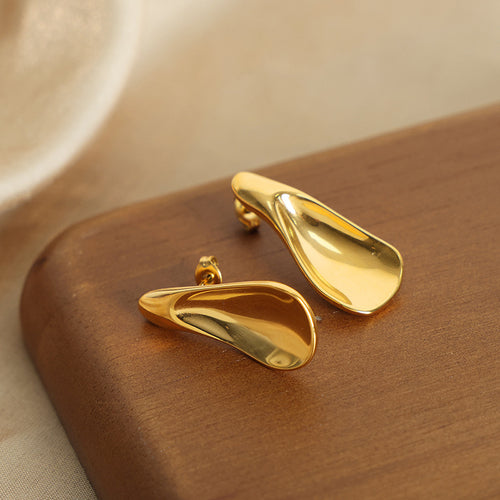 Pair of gold teardrop studs on wooden board side view