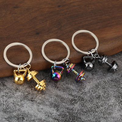 Three metal keychains display gold, rainbow, and gunmetal kettlebell and dumbbell charms.
