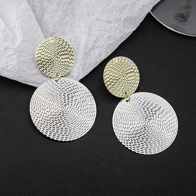 Gold over silver woven disc drop earrings on black crumpled paper