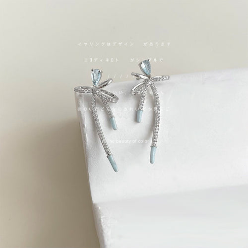 Silver light blue bow long drop earrings resting on white geometric block