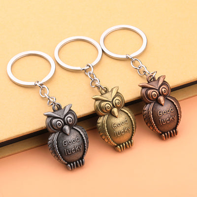 Three owl keychains in silver, bronze, and copper finishes on an orange surface.