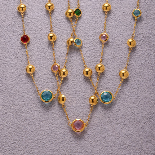 Flat lay gold ball station necklaces with multicolor glass on gray fabric