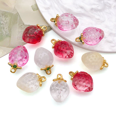 Close view of Translucent glass strawberry charms with gold tone loops showing the surface and openings