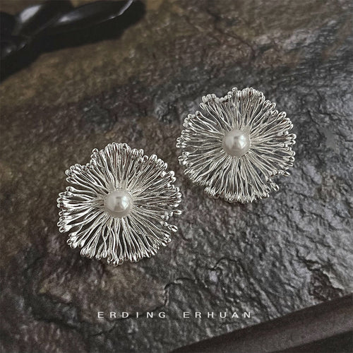 Silver-tone radiating wire flower and pearl studs on dark stone.
