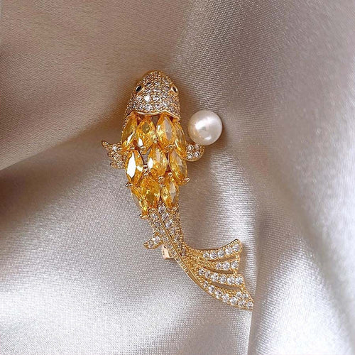 Close-up of gold koi brooch with yellow stones and pearl on silk