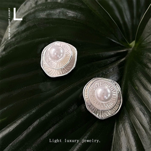 Silver layered ruffle disc pearl studs on dark green leaf