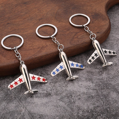 Three silver-tone airplane keychains with red, blue, and black stars rest beside a wooden board.